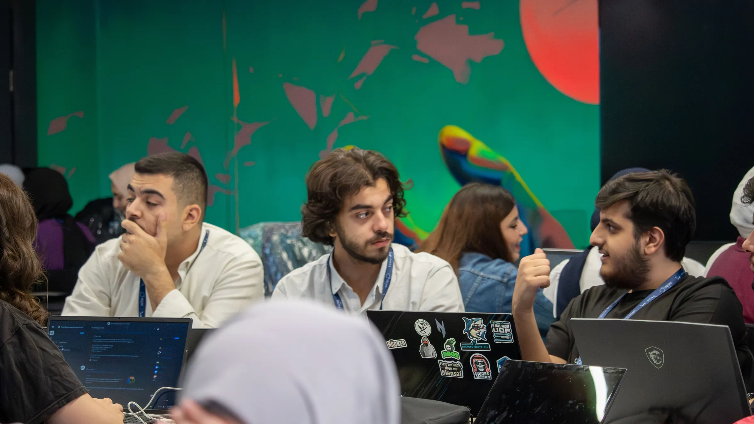 Participants working together at laptops in front of a colourful mural