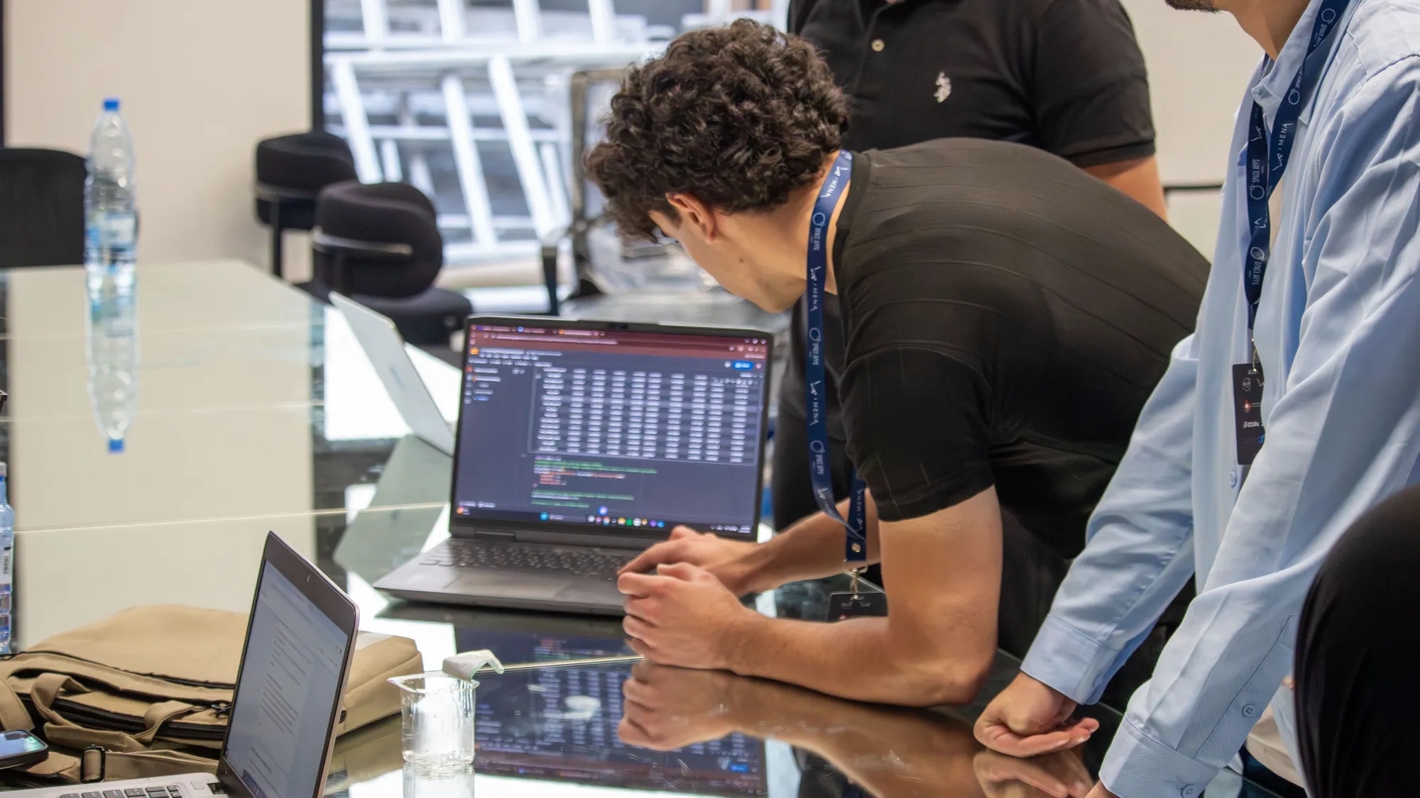 A participant leaning over a laptop showing code, watched by two others